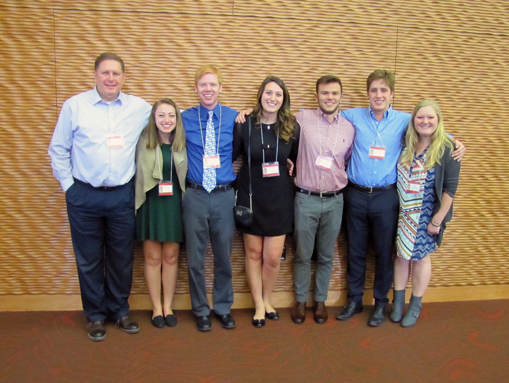 A group of students and staff pose for a picture with lanyards on.